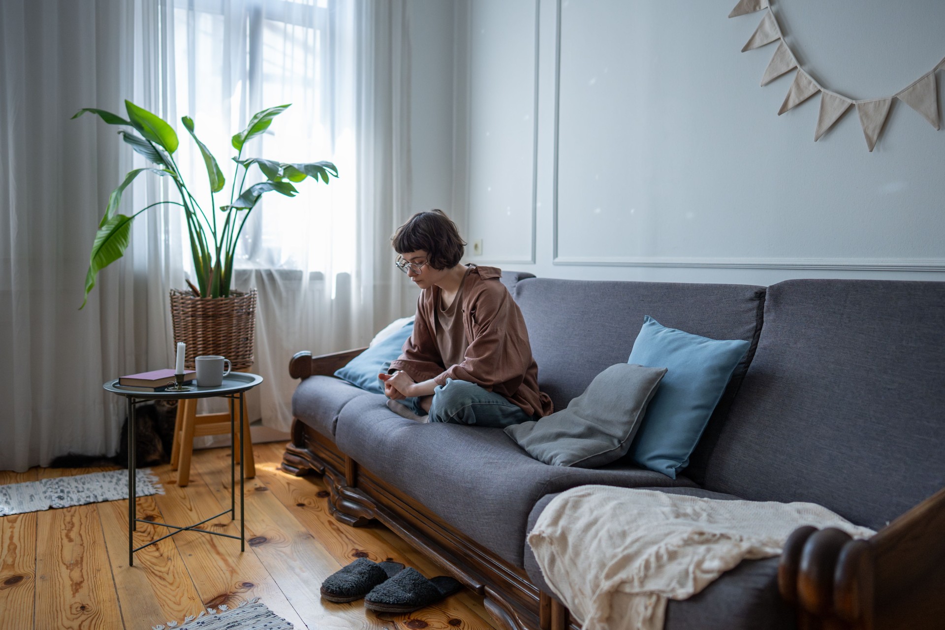 Bored sad girl sitting cross legged on sofa feels loneliness, uncertainty need of friendship support